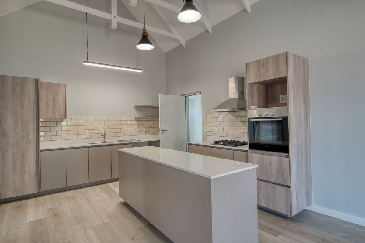 Modern kitchen featuring a central island, built-in oven, gas hob, extractor fan, and subway tile backsplash under a high vaulted ceiling.