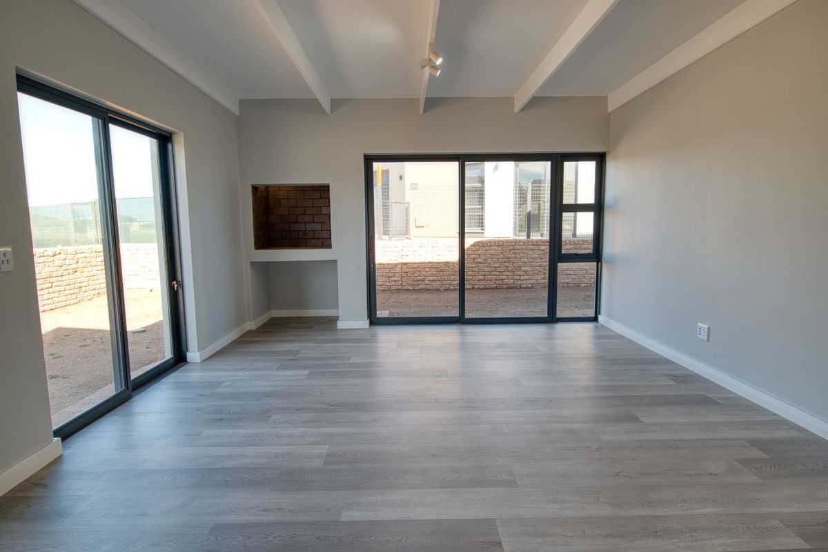 Bright and spacious living area featuring modern grey laminate flooring, exposed beam ceiling, and large sliding glass doors leading to the rear garden.