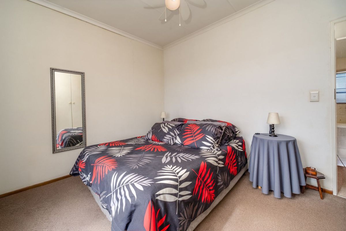 A standard bedroom featuring neutral walls, carpeted flooring, and a ceiling fan, with an adjacent view into a bathroom area.