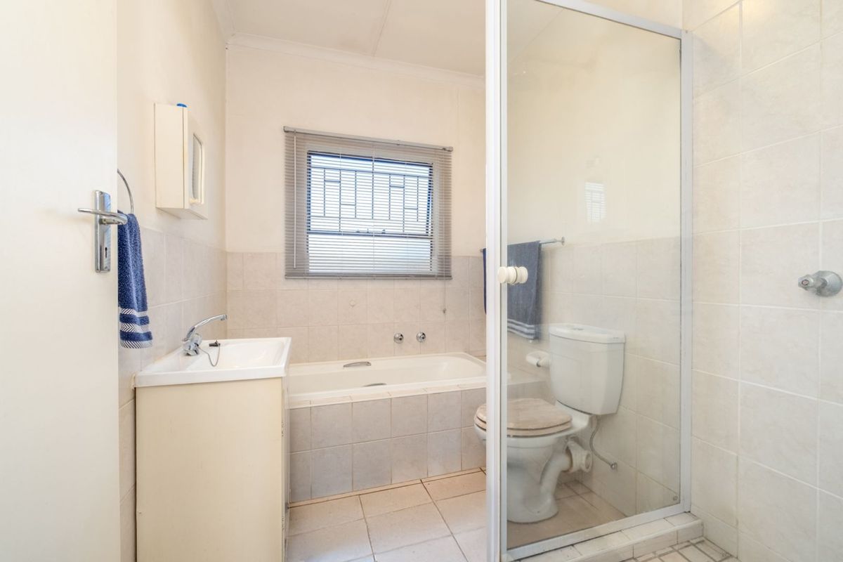 A functional bathroom featuring a built-in bathtub, a separate glass-enclosed shower, a pedestal vanity, and a toilet with neutral wall and floor tiling.