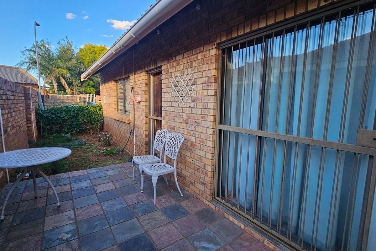 A private rear patio area featuring slate-style paving, face-brick exterior walls, and secure metal security gates over the sliding glass doors.