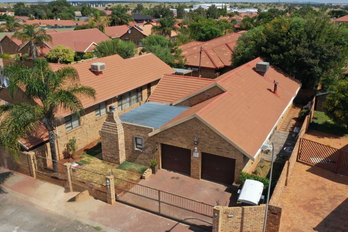 Aerial view of a brick-faced residential property featuring a double garage, tiled roof, and perimeter walling within a suburban estate setting.