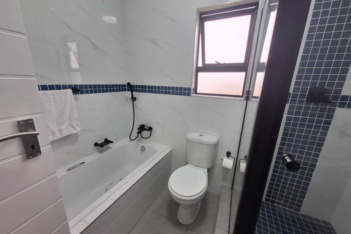Modern bathroom featuring a built-in bathtub, a separate shower enclosure with blue mosaic tiling, and a white ceramic toilet.