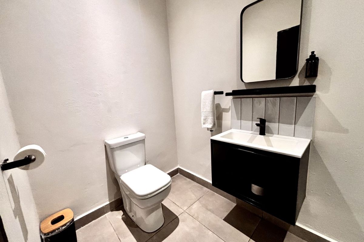 A modern guest bathroom featuring a wall-mounted vanity with a basin, a contemporary toilet, and a sleek mirror with tiled splashback.