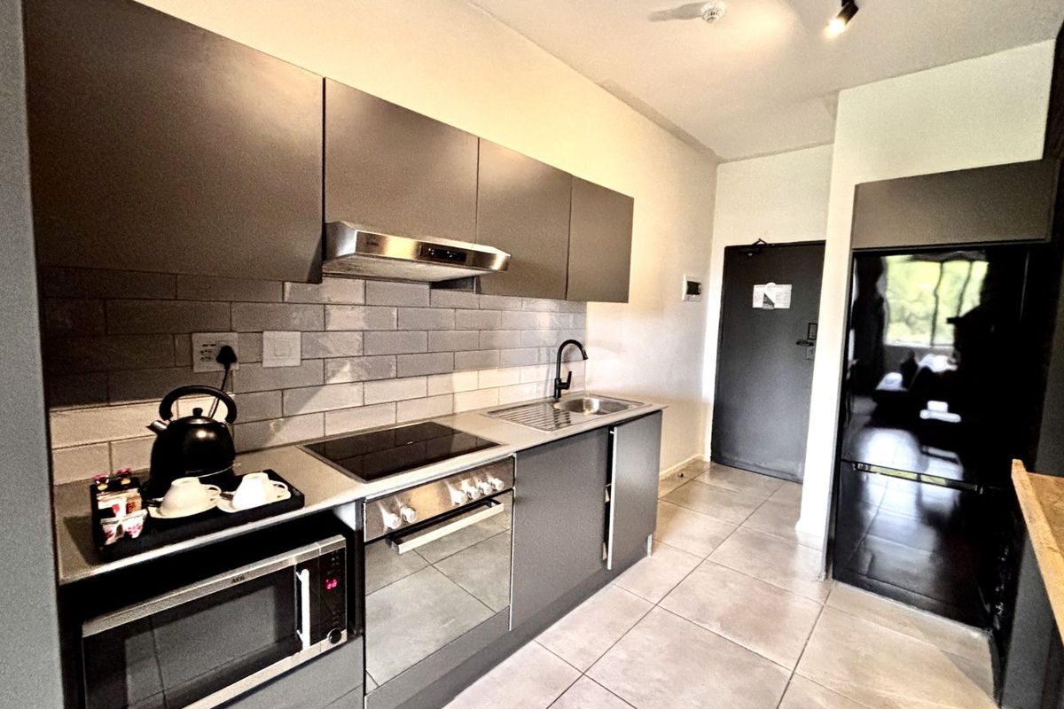 Modern kitchen featuring sleek grey cabinetry, subway tile backsplash, integrated oven, induction hob, extractor fan, and stainless steel sink.