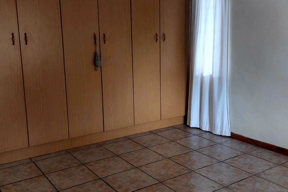 A bedroom featuring built-in wooden cupboards and tiled flooring, offering a functional and neutral space ready for personalization.