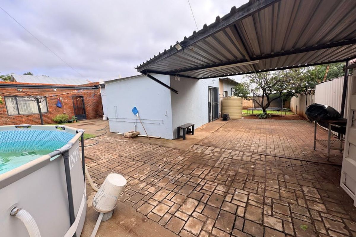Rear outdoor area featuring a paved patio with a covered carport structure, water storage tank, and space for a portable pool.
