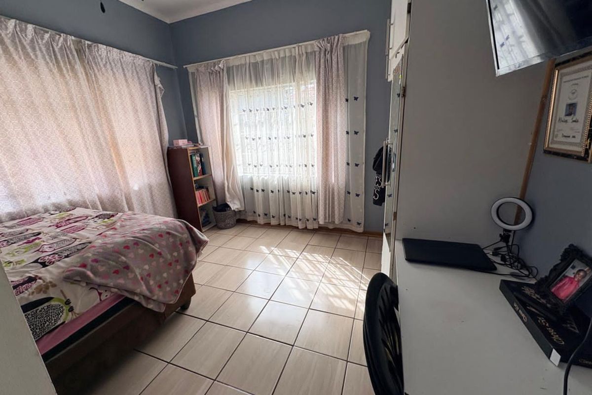 A well-lit bedroom featuring tiled flooring, built-in cabinetry, and large windows with curtain treatments.
