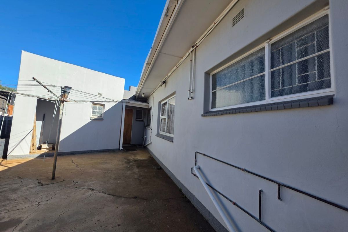 Rear exterior view of the property featuring a concrete courtyard, exterior wall finishes, and fixed utility piping.
