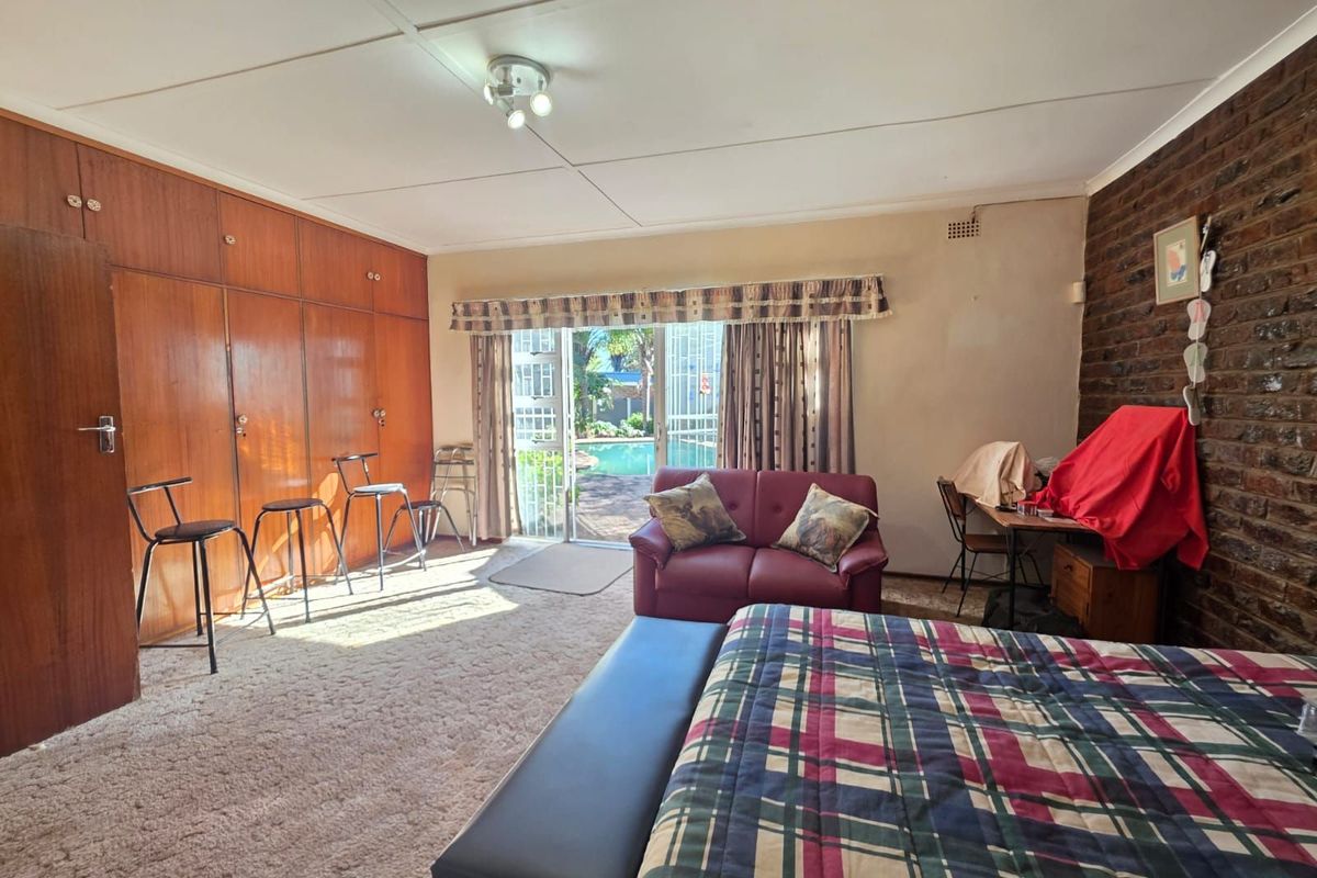 Spacious bedroom featuring extensive built-in wooden cabinetry, exposed brick feature wall, and sliding glass doors providing direct access to the outdoor pool area.