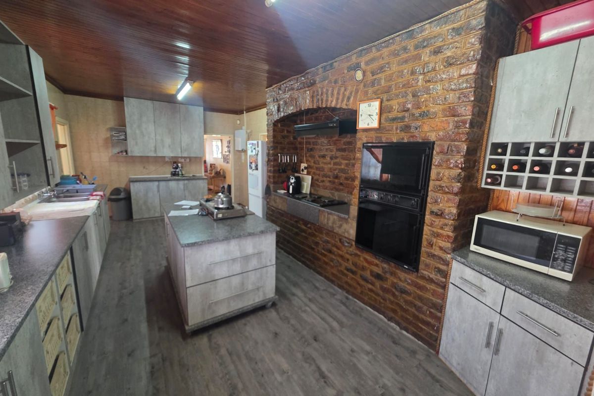 Spacious kitchen featuring a prominent brick feature wall, built-in oven, hob, central island, and modern grey cabinetry with wood-look flooring.