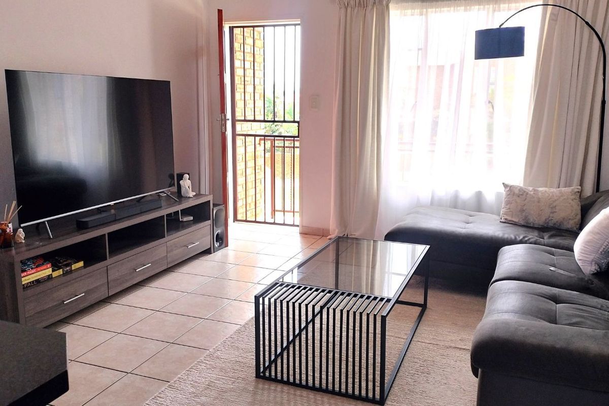 A living room featuring tiled flooring and a security gate leading to an outdoor balcony area.