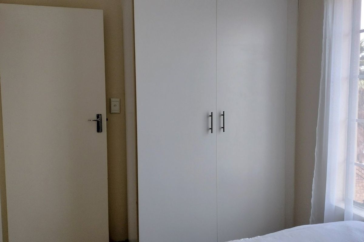 A bedroom featuring built-in cupboards with modern handles and a window allowing natural light into the space.