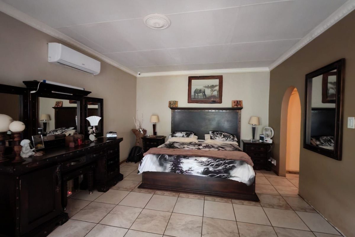 Spacious bedroom featuring tiled flooring, a wall-mounted air conditioning unit, and an arched doorway leading to an adjoining space.