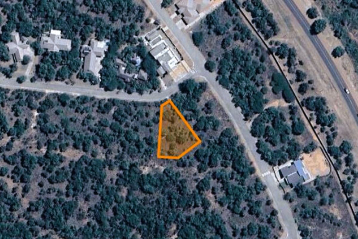 An aerial view of a vacant residential plot highlighted in orange, situated within a developed neighborhood with established vegetation.