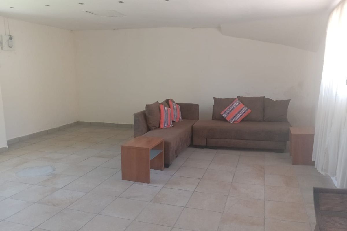 A spacious living area featuring neutral tiled flooring and recessed ceiling lighting, offering a blank canvas for interior design.