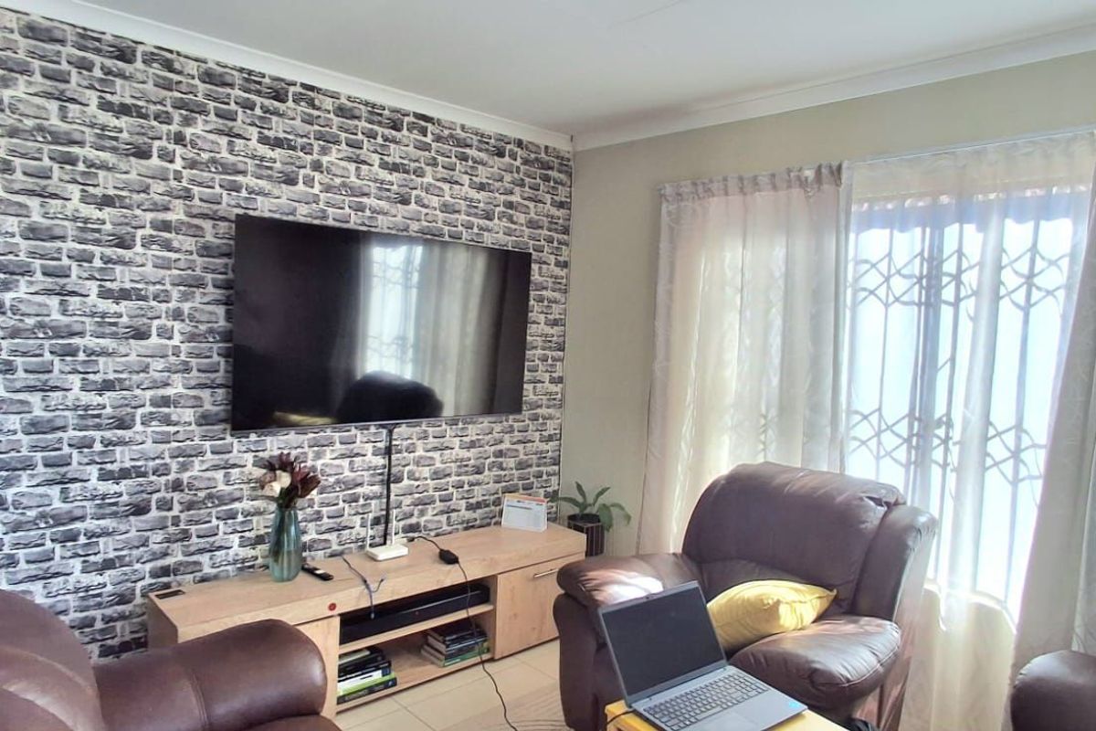 A comfortable living room featuring a brick-effect accent wall, tiled flooring, and a security gate on the window.