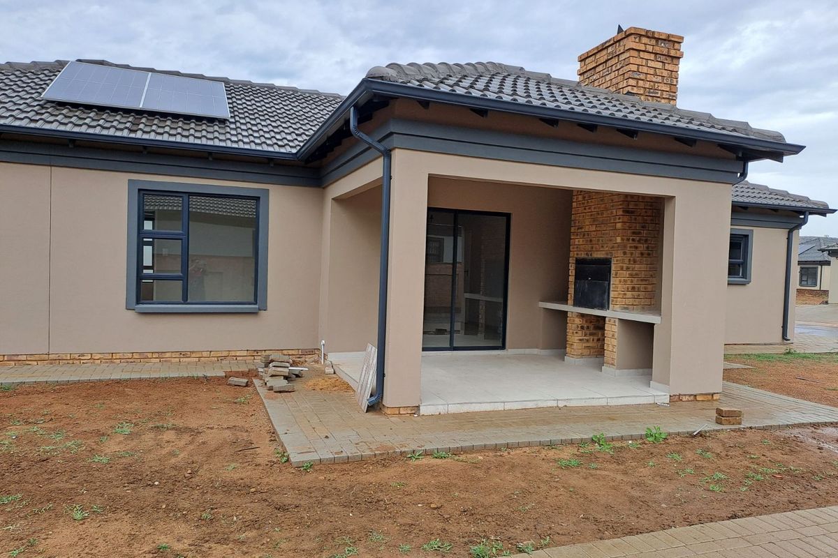 Rear view of the house featuring a covered patio with a built-in brick braai, tiled flooring, and solar panels installed on the roof.