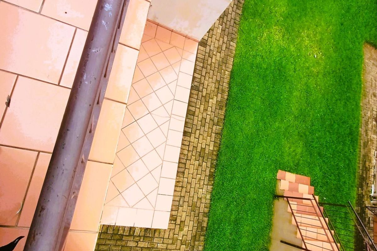 An elevated view of a tiled patio area with a metal railing, overlooking a small private garden with paved pathways.