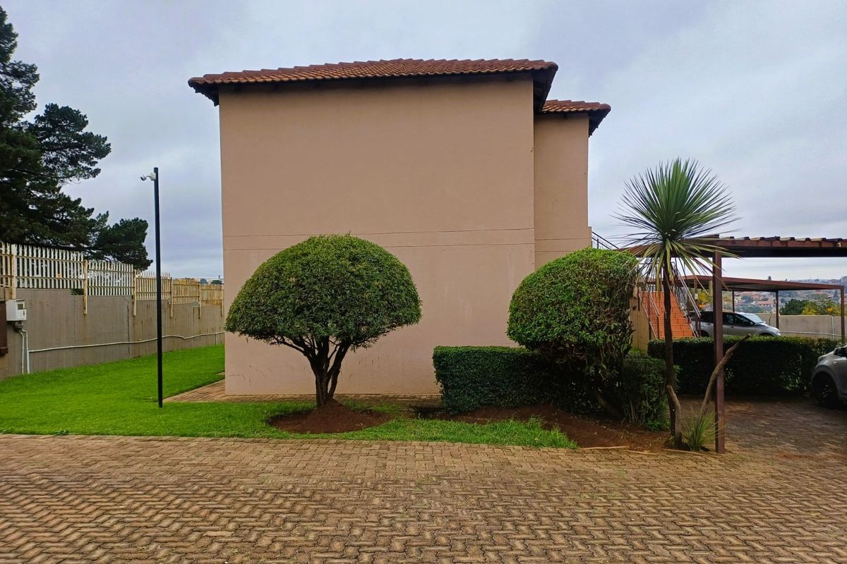Side view of the apartment building exterior featuring paved driveway, landscaped garden area, and covered parking structure.