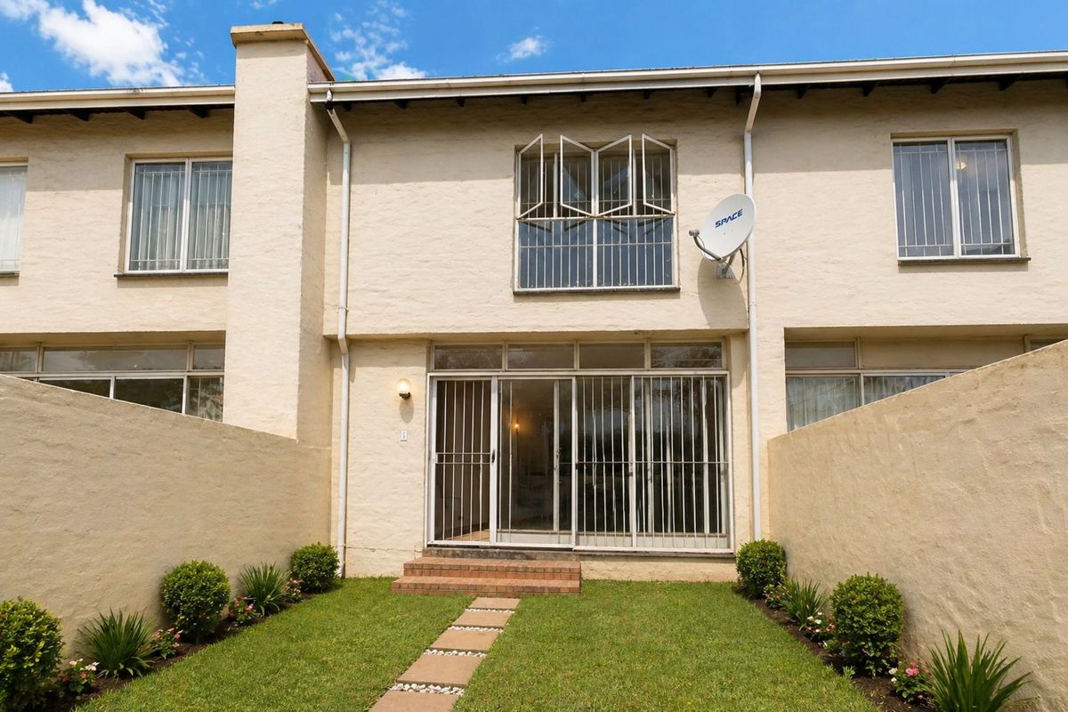 Rear view of a townhouse featuring a private garden, paved walkway, sliding glass doors with security gates, and upper-level windows with security bars.