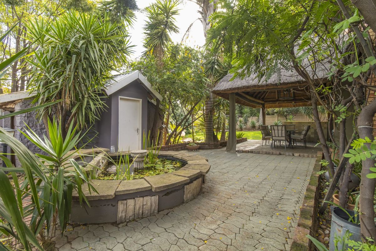 A landscaped rear garden featuring a paved patio area, a thatched gazebo, a stone water feature, and a small utility shed.