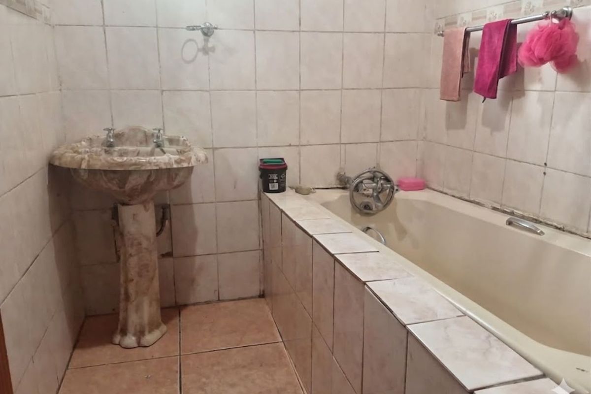 A dated bathroom featuring a pedestal basin, tiled bathtub surround, and wall-to-wall ceramic tiling.