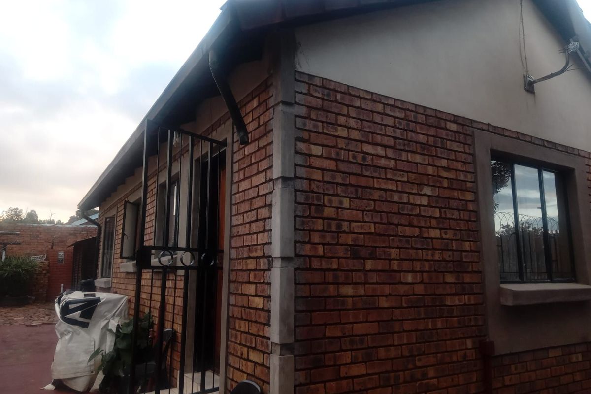 A side view of a face-brick residential property featuring security gates and tiled roof eaves.