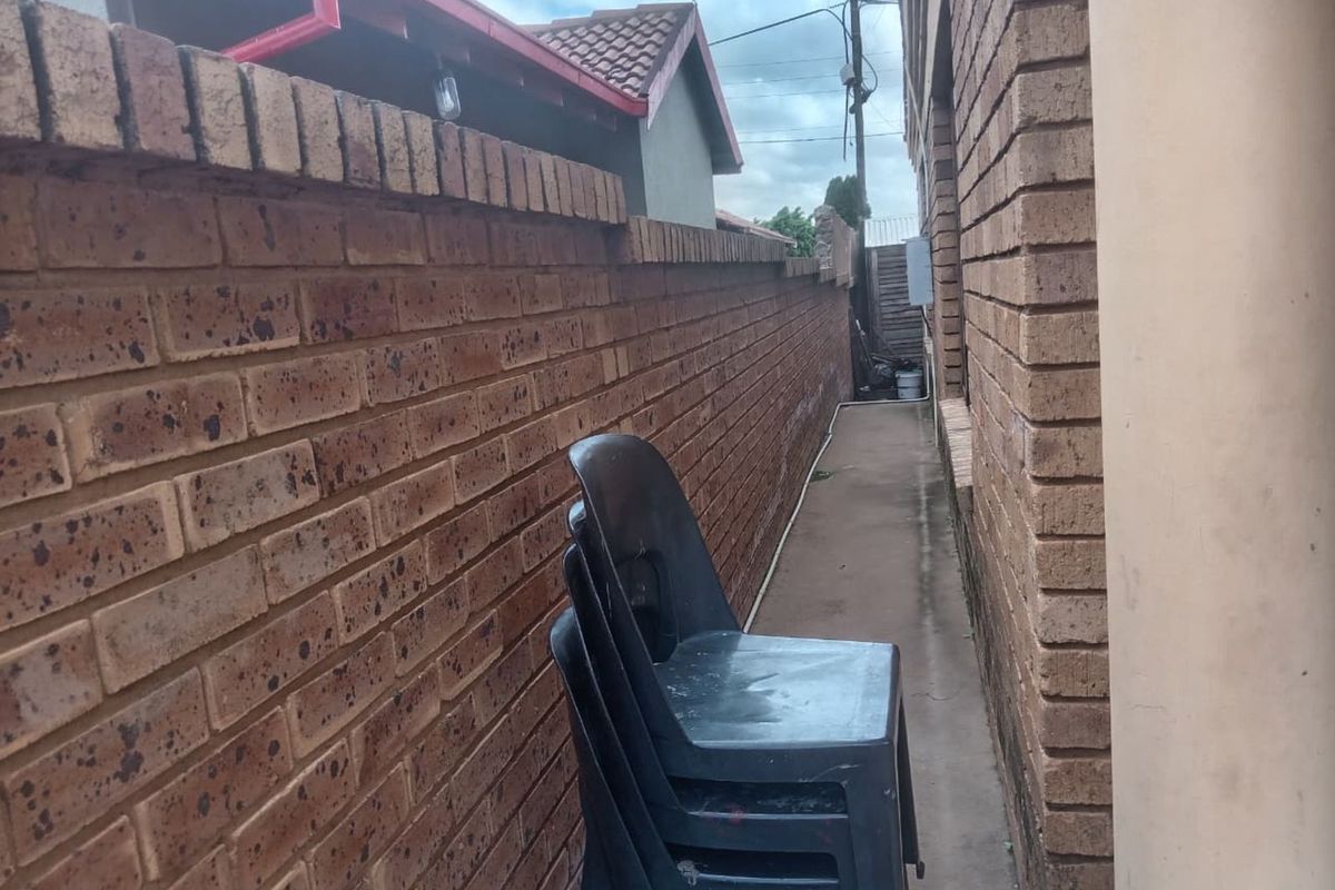 A narrow side passage between the exterior brick wall of the house and the boundary wall, featuring a concrete walkway.