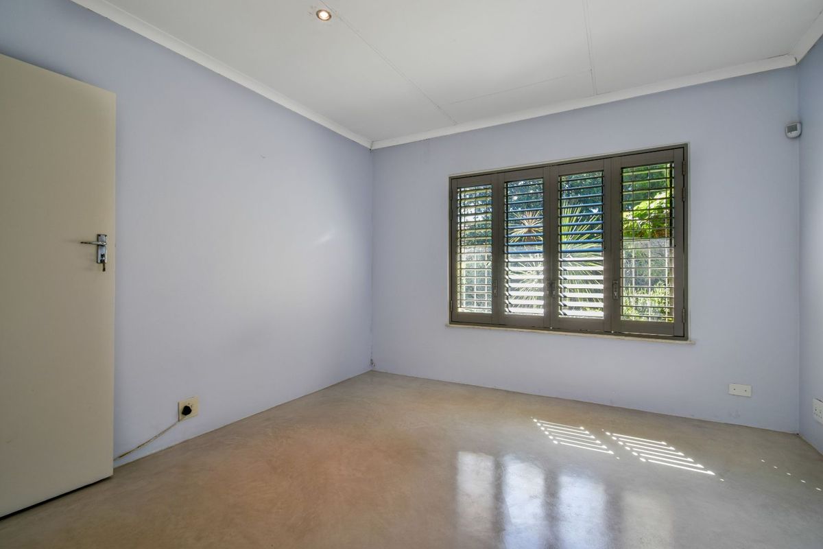 A bright, empty bedroom featuring polished concrete flooring, light blue walls, and fitted security shutters on the window.