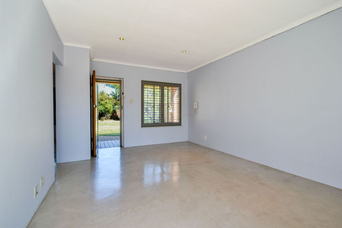 A bright, empty living room featuring polished concrete flooring, recessed ceiling lighting, and direct access to the rear garden through a glass-paneled door.