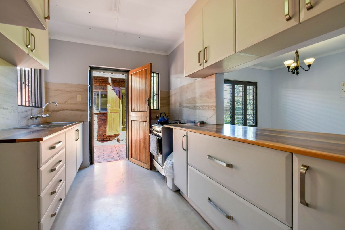 A functional kitchen featuring light-toned cabinetry, wood-look countertops, a stainless steel sink, and a freestanding stove, with direct access to an outdoor patio area.
