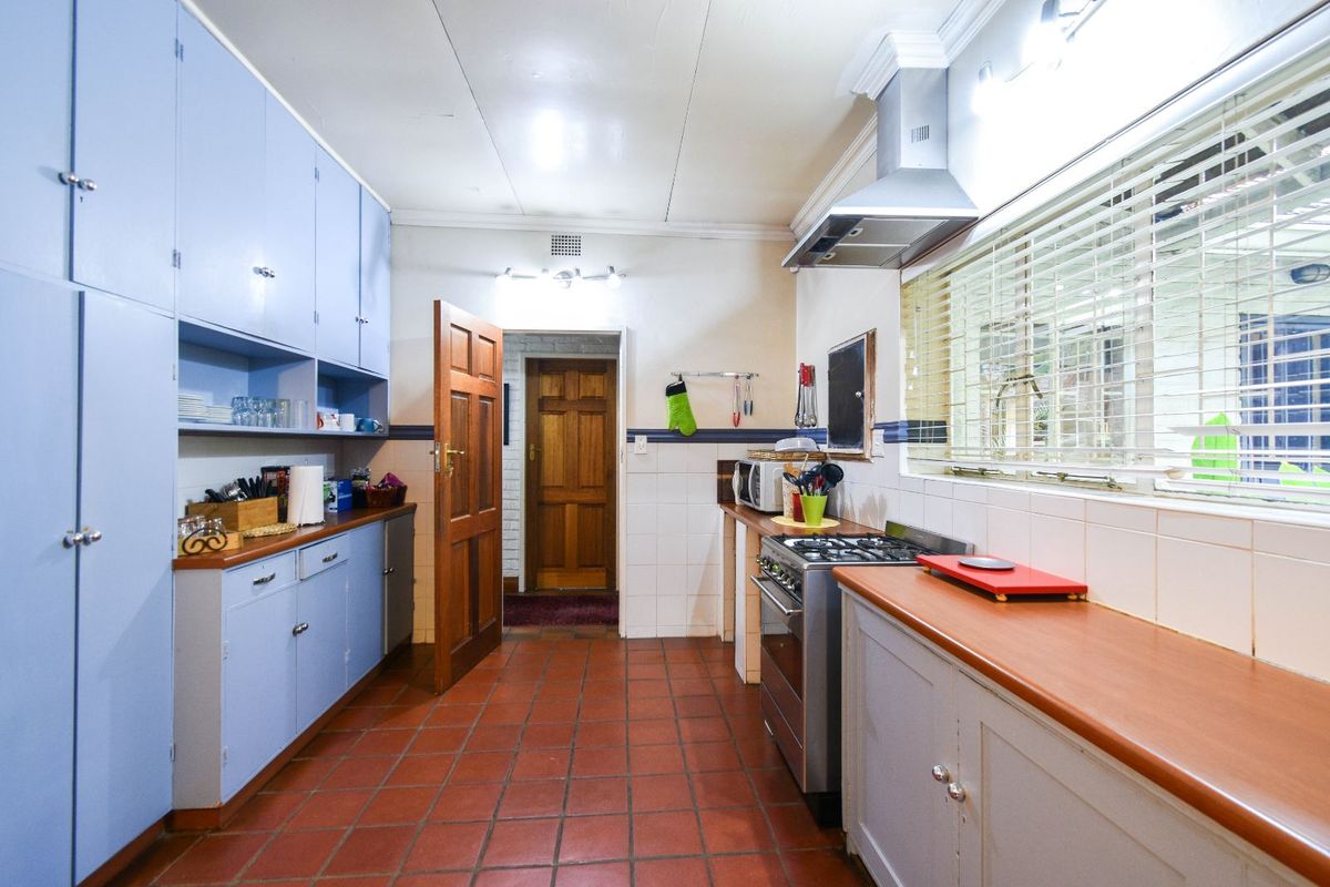 A functional kitchen featuring blue cabinetry, a gas stove with extractor fan, tiled flooring, and a window with fitted blinds.