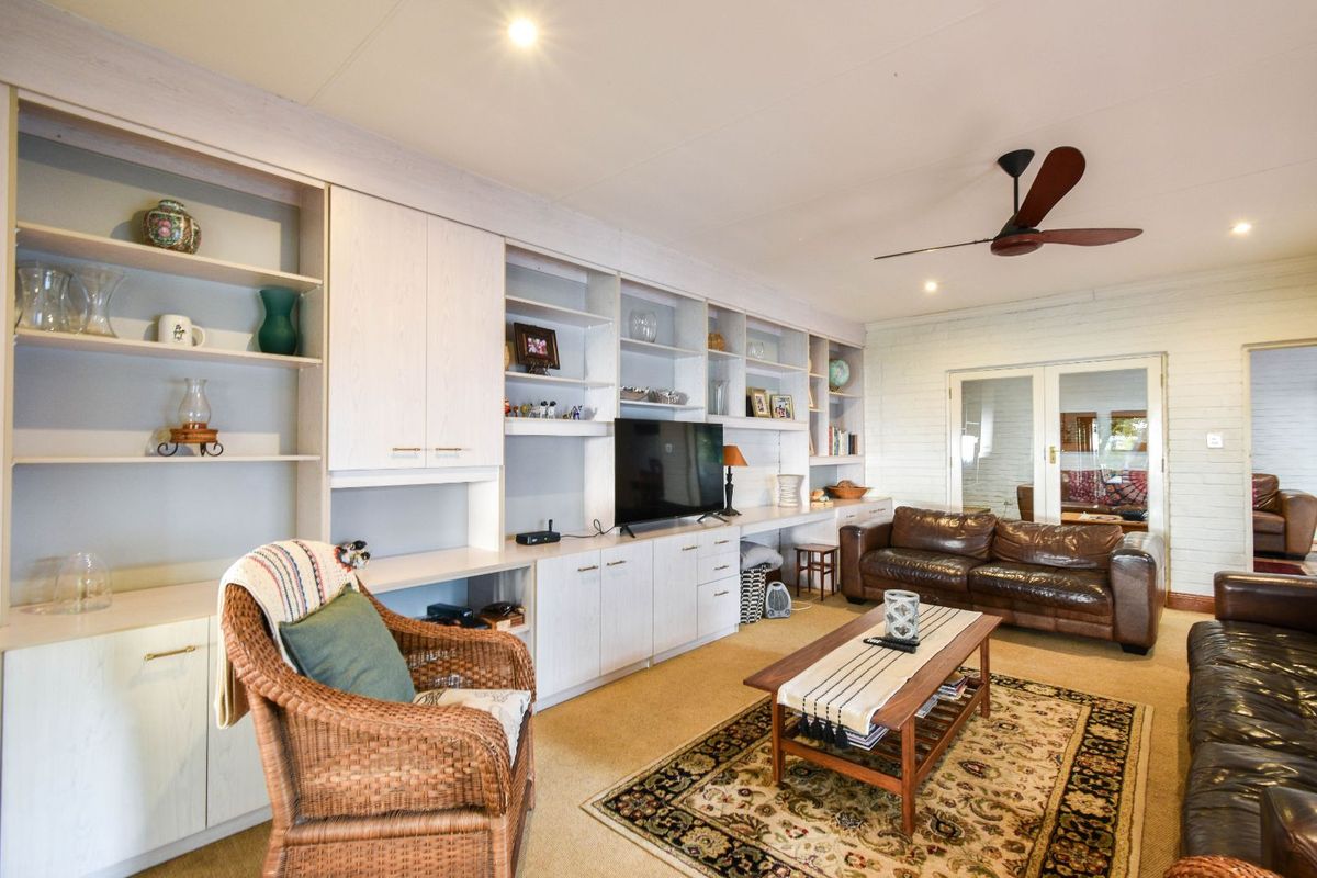 Spacious living room featuring extensive built-in cabinetry, shelving units, a ceiling fan, and glass-paneled double doors leading to an adjacent room.