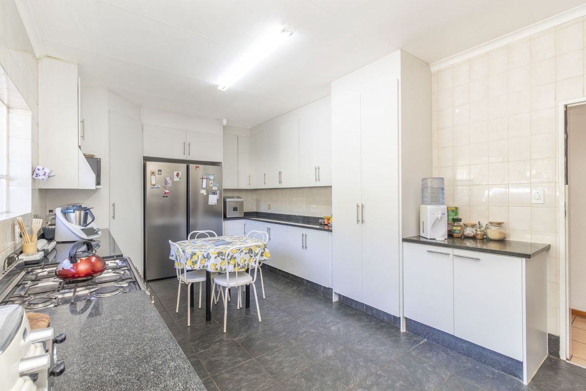 A functional kitchen featuring white cabinetry, dark granite countertops, a gas hob, and tiled flooring, offering ample storage and workspace.