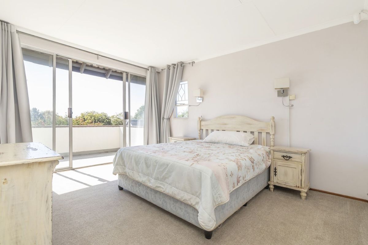Bright bedroom featuring neutral carpeting, wall-mounted lighting, and large sliding glass doors providing direct access to an outdoor balcony area.