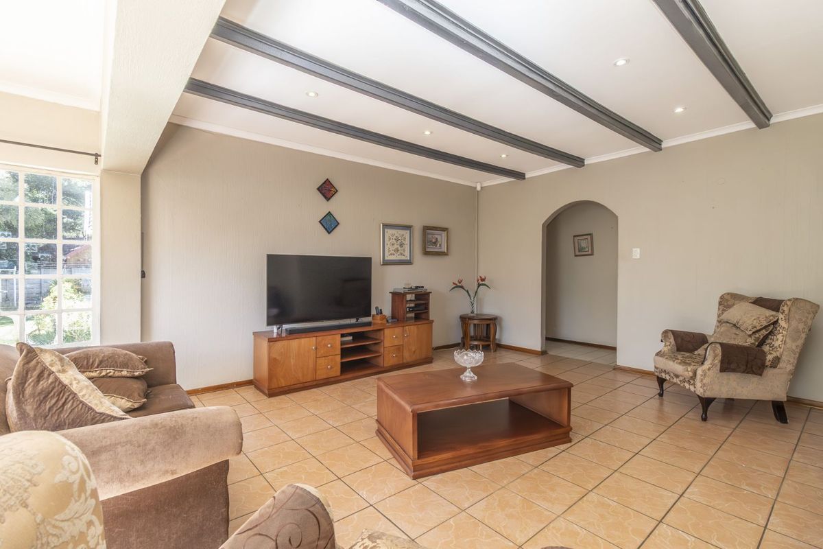 Spacious living room featuring tiled flooring, recessed ceiling lighting, and decorative exposed ceiling beams, leading to an arched hallway entrance.