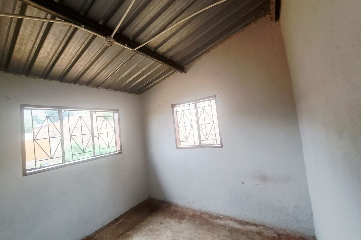 A basic, unfinished bedroom featuring exposed corrugated metal roofing, concrete flooring, and security-barred windows, offering a blank canvas for renovation.