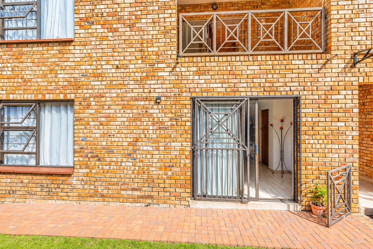 Rear exterior view of an apartment featuring a face brick facade, paved patio area, and secure metal sliding door access.