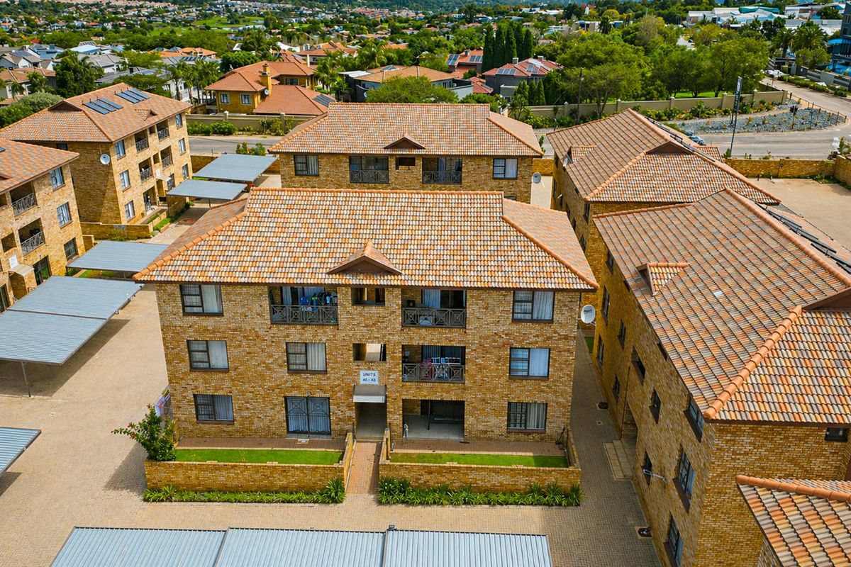 Aerial view of a multi-story apartment complex featuring face brick construction, tiled roofs, private balconies, and dedicated covered parking areas.