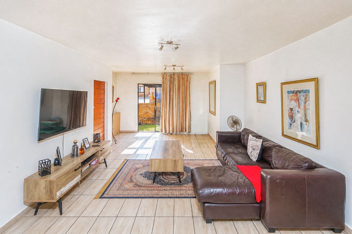 A spacious living room featuring tiled flooring, track lighting, and a sliding glass door providing access to the outdoor area.
