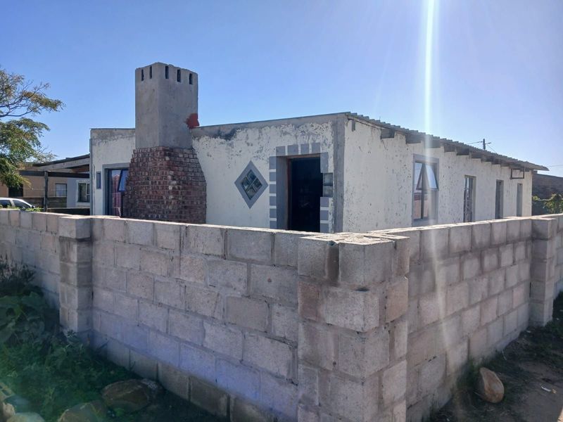 Exterior view of a single-story house featuring a prominent brick chimney, concrete block boundary wall, and unfinished exterior wall finishes.