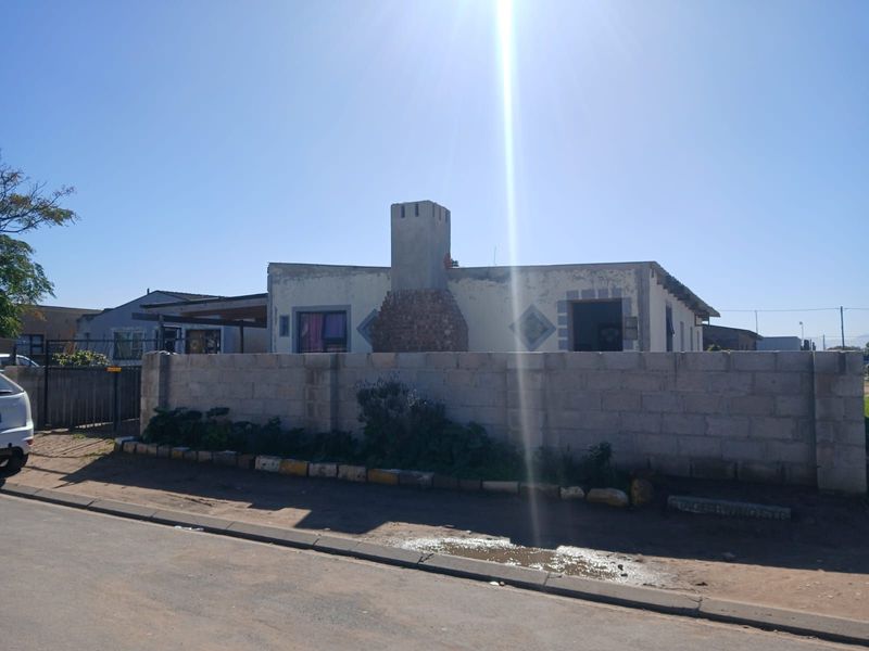 Front view of a single-story house featuring a prominent brick chimney and a concrete block boundary wall.
