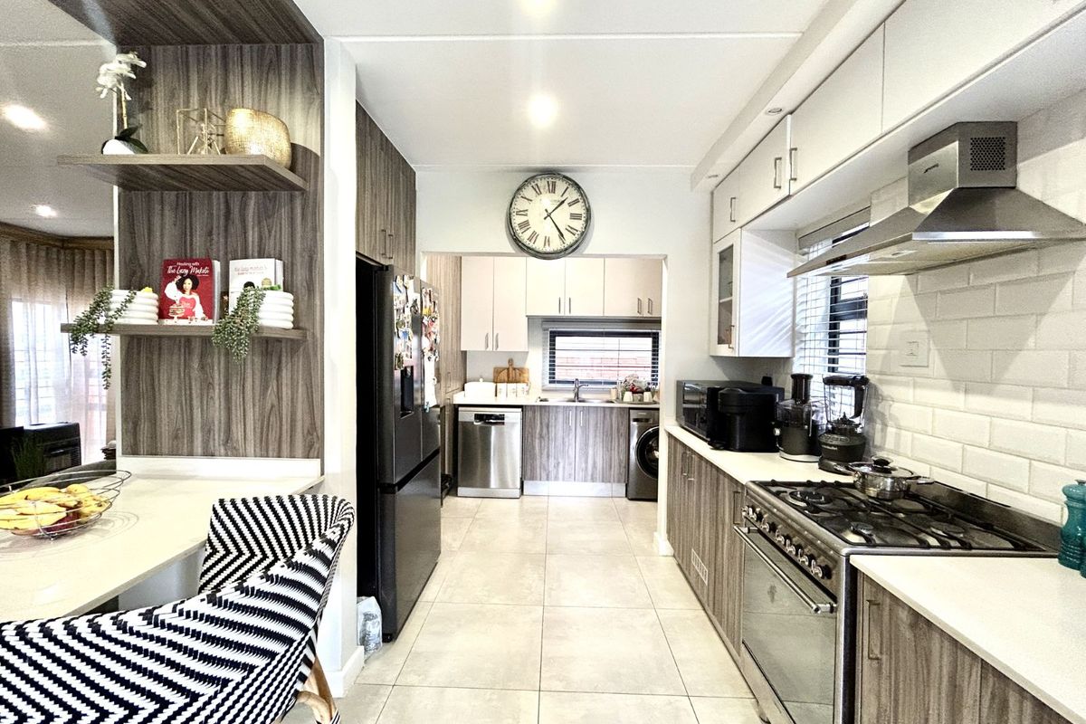 Modern kitchen featuring wood-grain cabinetry, white subway tile backsplash, stainless steel gas stove, extractor fan, and integrated appliance spaces.