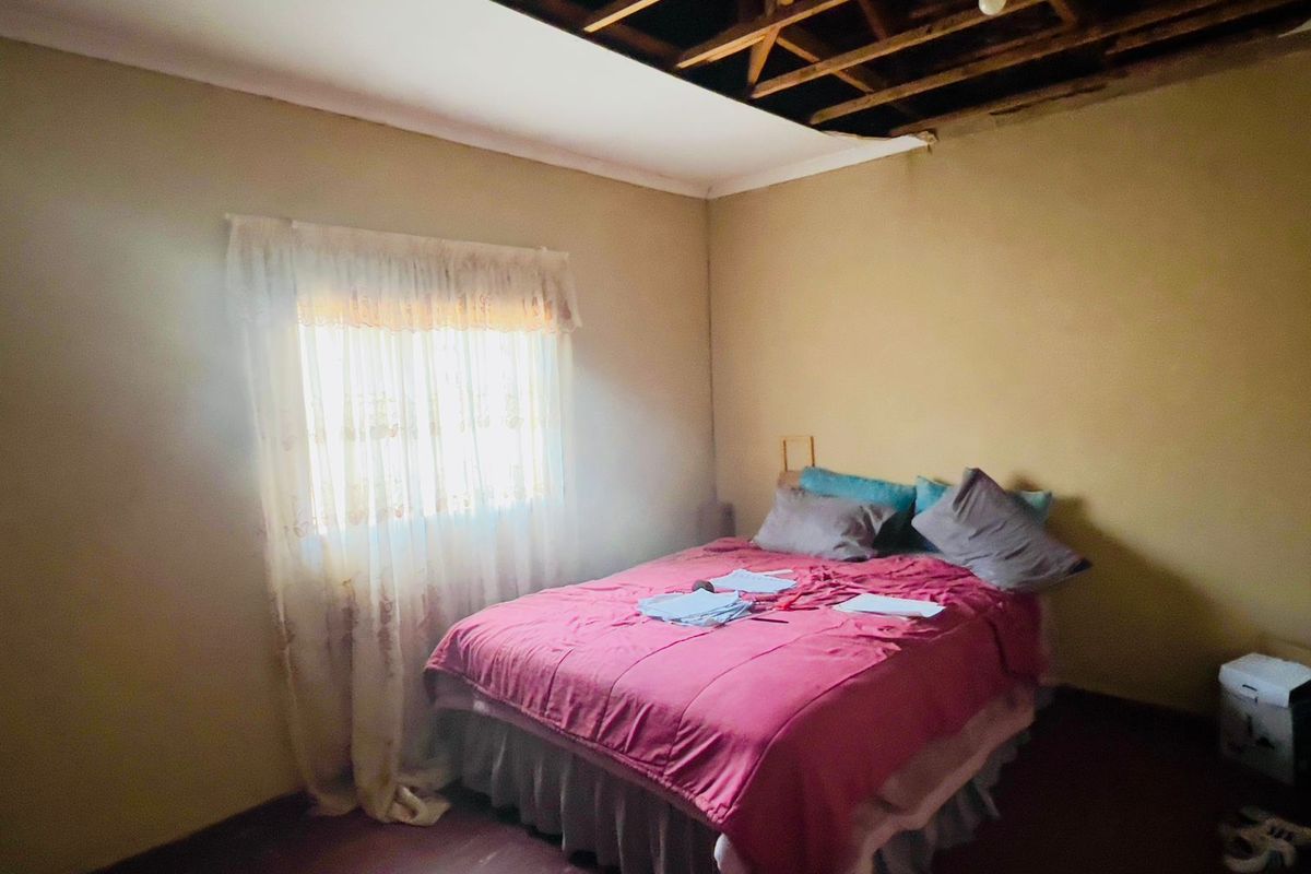 A bedroom featuring exposed roof trusses and missing ceiling sections, requiring repair and renovation to restore the interior finish.