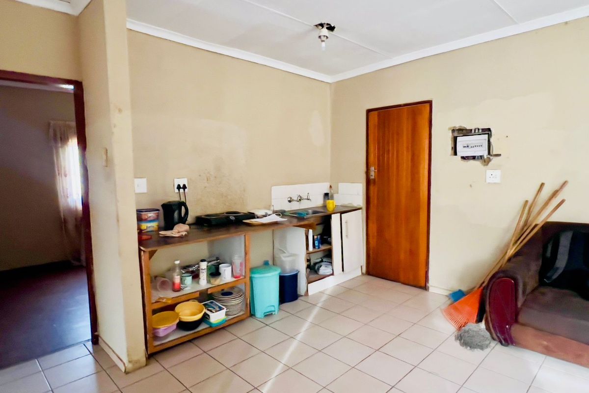 A basic kitchen area featuring tiled flooring, a simple sink unit with open shelving, and exposed wall sections requiring maintenance and renovation.