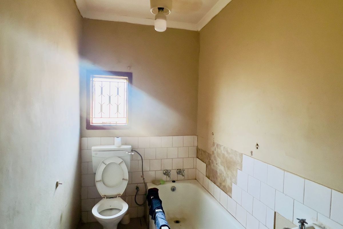 A dated bathroom featuring a standard bathtub, toilet, and basin, currently requiring significant renovation and repair to wall finishes and ceiling.
