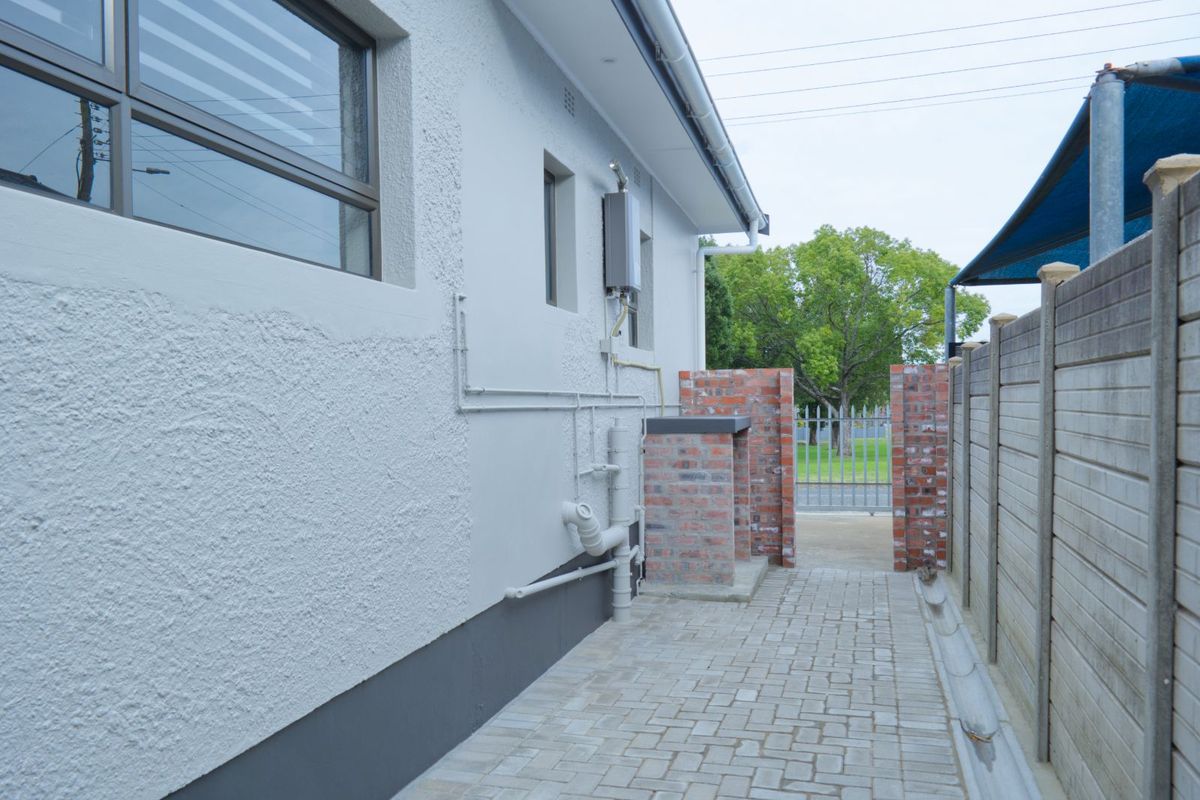 A side exterior view of the apartment featuring paved pathways, brick boundary walls, and external plumbing fixtures.