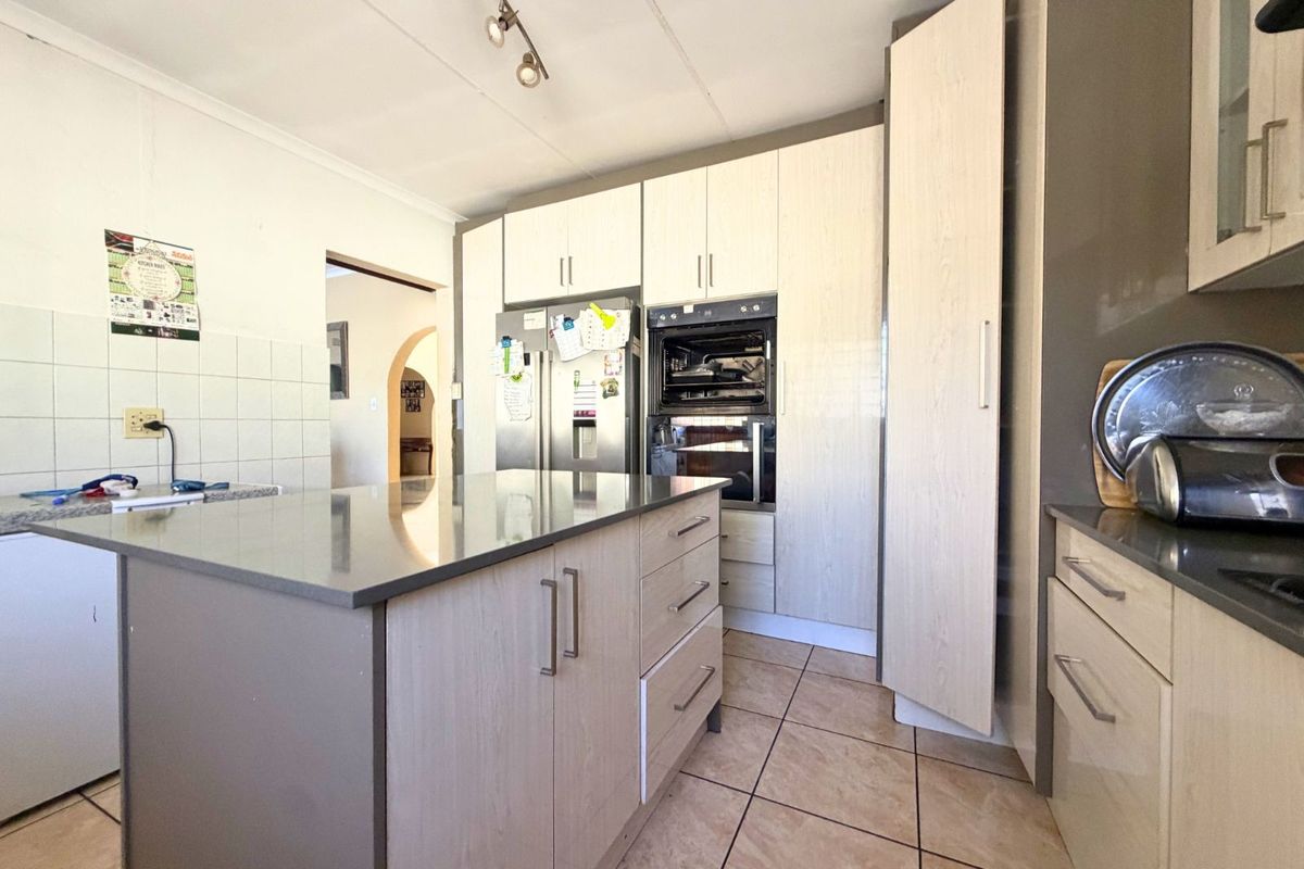 Modern kitchen featuring a central island, built-in oven, ample cabinetry, and tiled flooring, offering a functional workspace with a clean, contemporary layout.