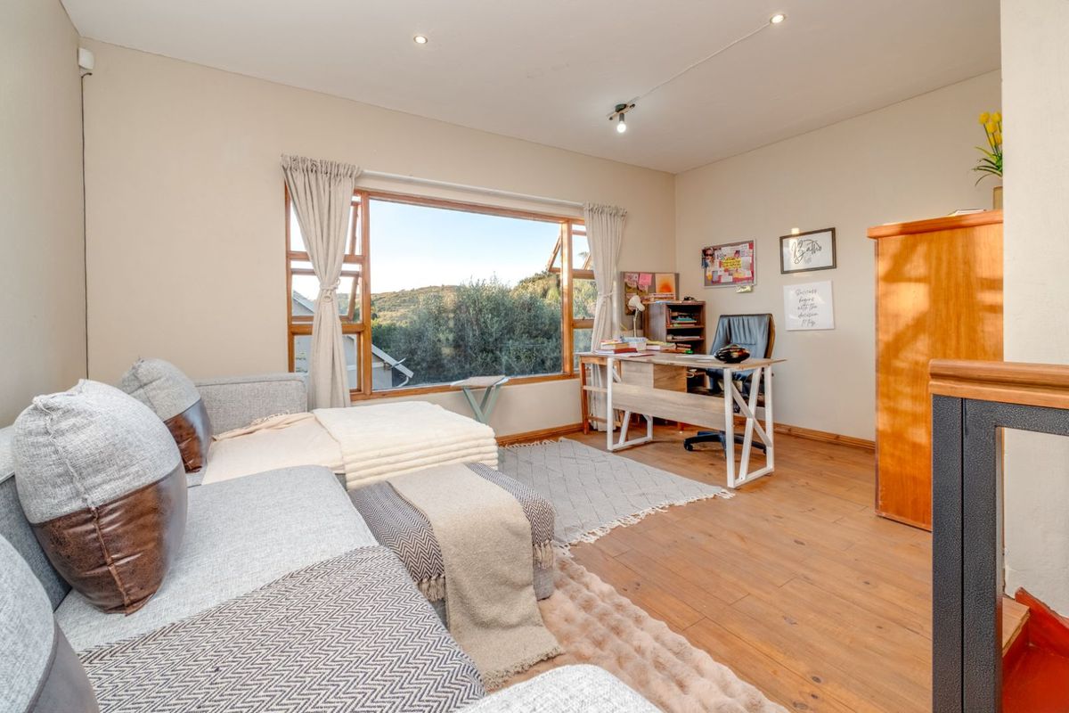 A bright living area featuring warm timber flooring, recessed downlighting, and a large window offering scenic views.